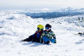 Two young children, siblings brothers, skiing in Austrian mountains on a sunny day