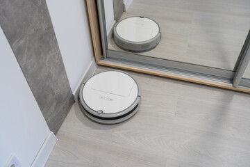 Robotic vacuum cleaner on laminate wood floor in bedroom.