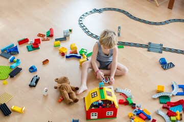 Cute child, playing with colorful toy blocks. Little boy building house of block toys sitting on...