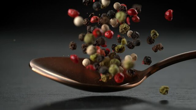 Colorful Peppercorns on Metal Tablespoon Falling onto Stone Kitchen Board
