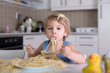 Little blond boy, toddler child, eating spaghetti for lunch and making a mess at home in kitchen