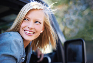 Feeling carefree outdoors. A young woman feeling the breeze in her hair through an open car window.