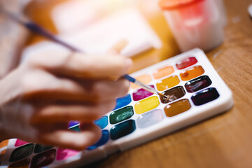 Hand with brush for drawing over multi-colored palette of watercolor paints. Theme of creativity...