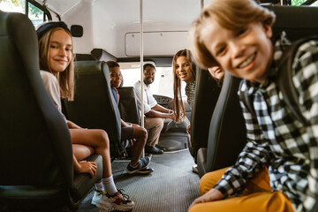 Black driver and multiracial pupils smiling while sitting in school bus