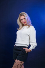 Portrait of a young woman with blond hair in a white sweater on a blue background in the studio.