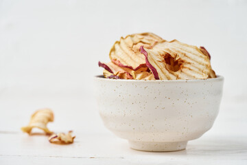 Dried apple chips in a bowl and pieces of this fruits on a white background. Horizontal orientation, copy space.