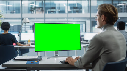 Close Up Over the Shoulder Shot of a Businessman Working on Desktop Computer with Chroma Key Green Screen Mock Up Display. Digital Projects Manager Typing Data, Using Keyboard and Mouse.