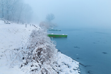 Snow covered lake shore in december with green fishing boats on the shore