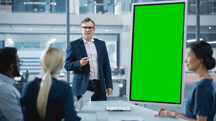 Company Operations Manager Holds Meeting Presentation for a Team of Economists. Adult Male Uses Digital Whiteboard with Vertical Green Screen Mock Up Display. People Work in Business Office.