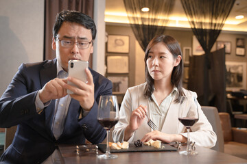 食事中にスマートフォンを操作する男性と呆れる女性