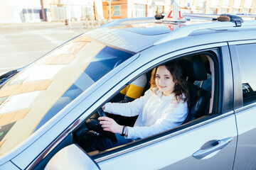 Smiling young woman in drivers seat of car taking driving lesson from instructor. Driving school concept.