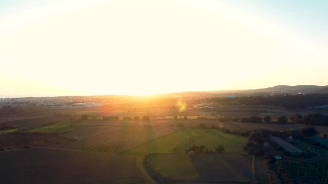 Atardecer con luz naranja de puesta de sol en el horizonte bajo prados verdes de hierba y la ciudad de Vilanova y su mar al fondo