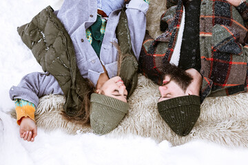 couple of young woman and man lying on snow under tree in courtyard in winter, concept of Christmas and New Year vacation on farm, family love and support, Valentines Day celebration