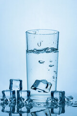 ice cube falls into a glass of water. Glass of water with ice cubes on a light blue background.