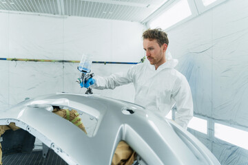 Young curly car painter varnishes a car bumper. Man works in a spray booth. Process of painting car...