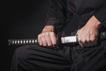 The samurai holding a Japanese katana sword. Photo of a warrior dressed in black clothes in low key...