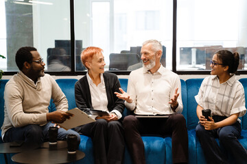 Multiracial colleagues talking and using gadgets during meeting