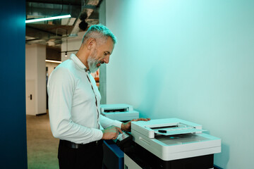 Mature man using copy machine while working in office