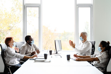 Multiracial colleagues in face masks talking during meeting at office