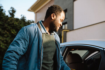 Black beard man getting out of his car on parking by house