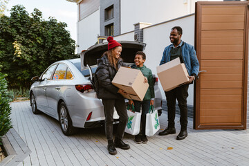 Black family standing with cardboard boxes on parking during moving