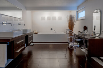 Modern bathroom in white and brown with two sinks, bathhub  and wooden furniture.