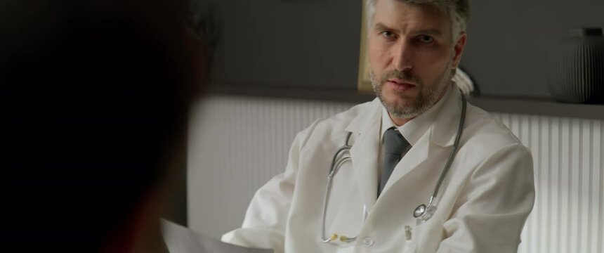 Portrait of stressed supportive Caucasian doctor delivering bad news to his patient during the visit. Shot with 2x anamorphic lens