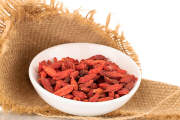 Dried sweet goji berries with white ceramic saucer and jute napkin, macro, isolated on white.