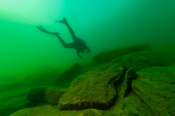 SCUBA diver exploring a cloudy inland lake with large boulders