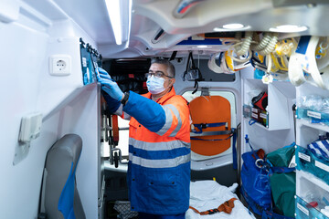 photo of a middle-aged doctor with gray hair checking the material in the ambulance cabinet