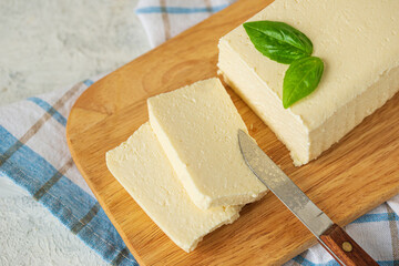 tofu, paneer, soy cheese, curd cheese, brynza, feta, Adyghe cheese with Basil and a knife on a wooden cutting Board on a light background