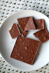 Almond and hazelnut chocolate bar on a plate and soft knited blanket. Top view.