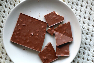 Almond and hazelnut chocolate bar on a plate and soft knited blanket. Top view.