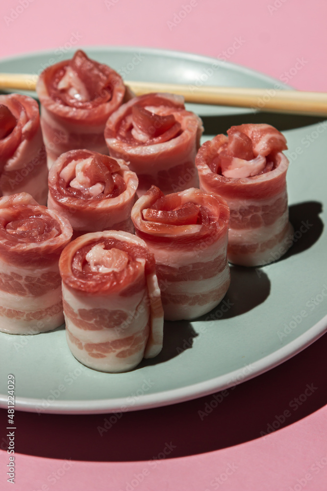 Wall mural Bacon on a pink background. Raw bacon on a plate. Chinese sticks next to pieces of meat. Pig meat. rolled bacon