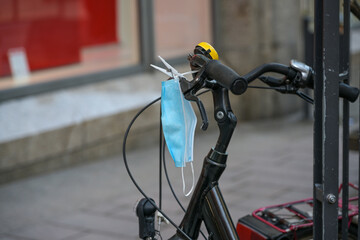 Surgical face mask hanging with a clothespin on a bicycle handlebar ready to be used in the city,...