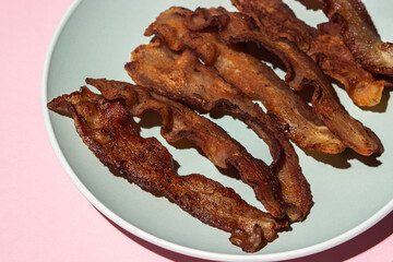Fried bacon on a pink background. Bacon fried until crispy. Pig meat.