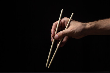 Hands holding Chinese chopsticks on a black background. Traditional wooden Chinese sticks.