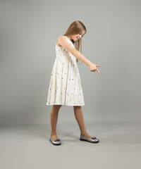 A beautiful girl smiles and points to the copy space. A young woman in a casual dress on a gray background