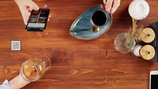 Scanning QR code in restaurant top view. Woman using qr code with smartphone, online menu in cafe. Modern technology, ordering meal in application. Contactless touch-free payment in app.