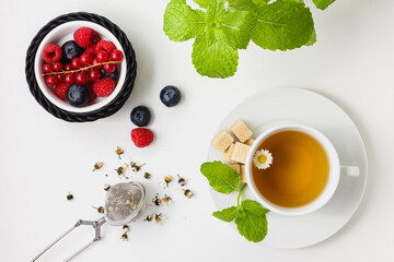 Chamomile tea with mint and berries in black basket on white background.