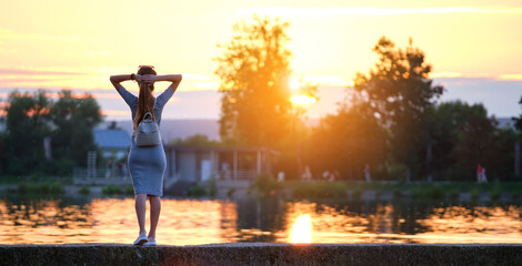 Young woman in casual outfit relaxing on lake side on warm evening. Summer vacations and travelling concept