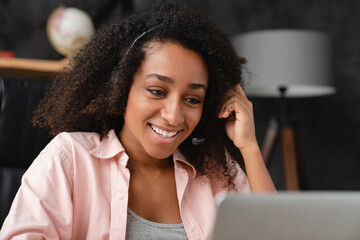 Smiling friendly young african student woman IT support customer support manager in headset using laptop, working remotely, having video call conversation conference online