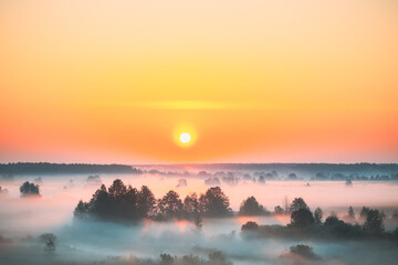 Amazing Sunrise Sunset Over Misty Landscape. Scenic View Of Foggy Morning Sky With Rising Sun Above Misty Forest And River. Early Summer Nature Of Eastern Europe