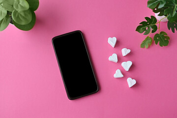 White marshmallow hearts and smartphone on pink pastel background. Concept of acquaintance, love in...