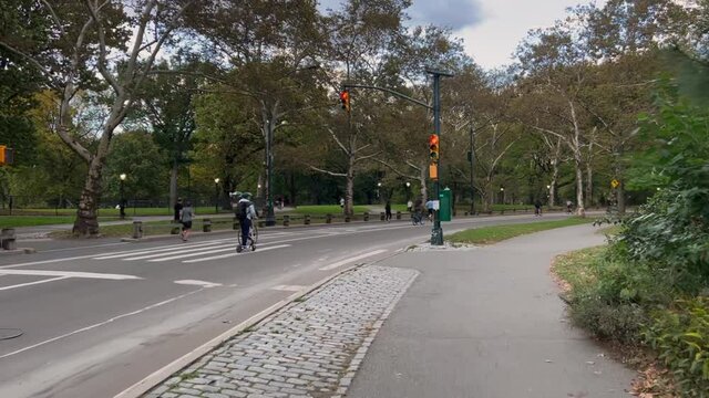 Central Park in New York. People walk along the path, ride bicycles, jogging.