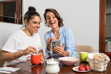 Homosexual family having breakfast while watching the mobile phone and laughing together at home