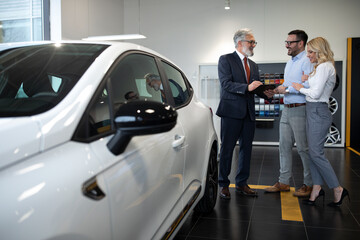 Vehicle purchase. Happy car buyers handshaking with auto seller standing among luxury automobiles...