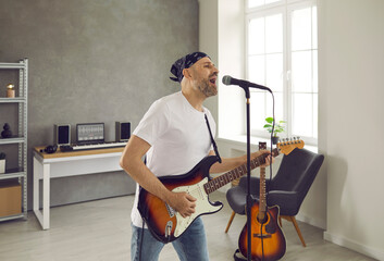 Rock musician rehearsing his new song in his studio. Middle aged man standing in rehearsal room,...