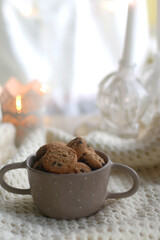 Bowl of chocolate chip cookies, soft blanket and candle holders with lit candles. Hygge at home. Selective focus.