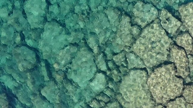 Top view blue clean sea water with rocky bottom, aerial. Static shot. beautiful texure